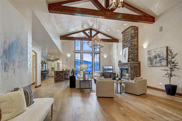 living room featuring hardwood / wood-style floors, beam ceiling, high vaulted ceiling, a stone fireplace, and a chandelier