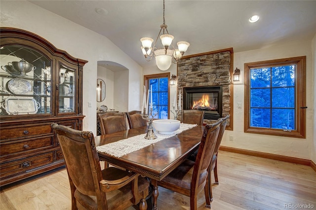 dining area with lofted ceiling, a stone fireplace, light hardwood / wood-style floors, and a notable chandelier