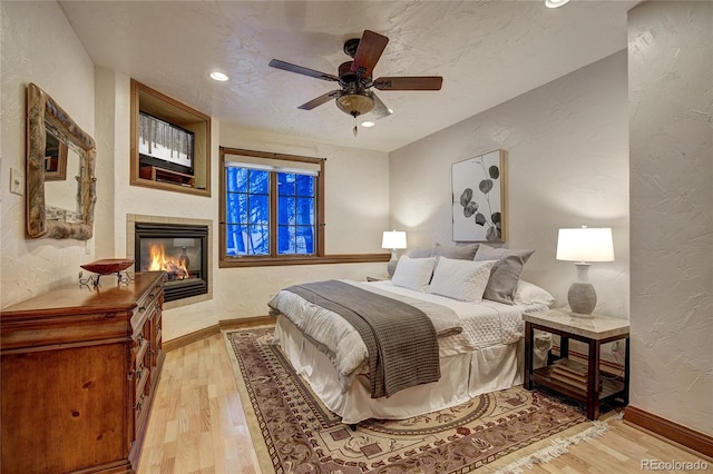 bedroom with a tiled fireplace, ceiling fan, a textured ceiling, and light wood-type flooring