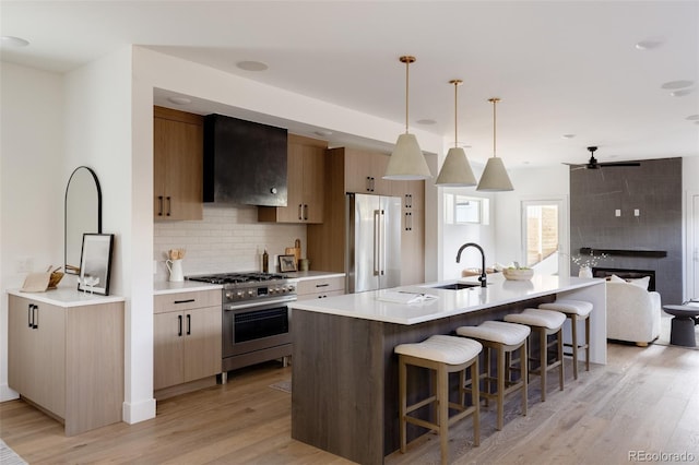 kitchen with sink, wall chimney exhaust hood, premium appliances, backsplash, and decorative light fixtures