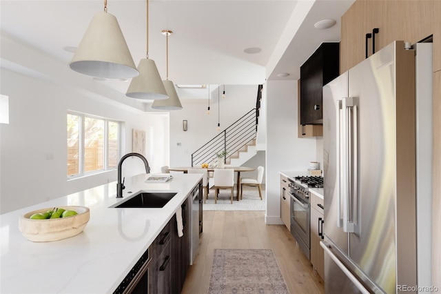 kitchen featuring high end appliances, sink, hanging light fixtures, light wood-type flooring, and light stone countertops