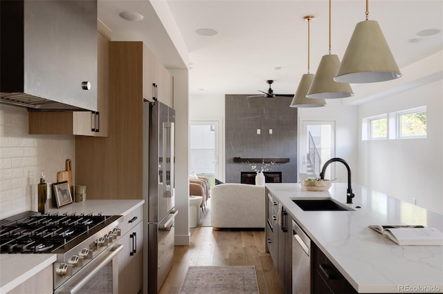 kitchen with wall chimney range hood, sink, hanging light fixtures, light stone countertops, and premium appliances