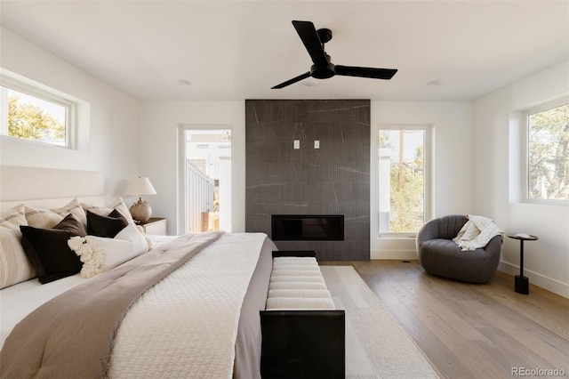 bedroom featuring multiple windows, light hardwood / wood-style floors, ceiling fan, and a tiled fireplace