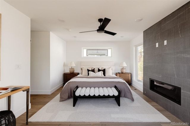 bedroom with ceiling fan, a tile fireplace, and light hardwood / wood-style flooring