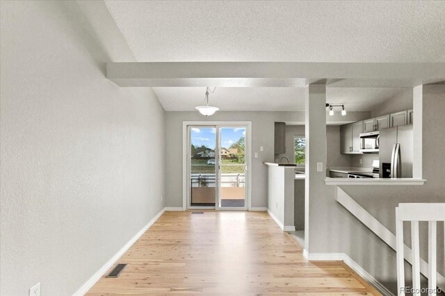 13244 Quivas St, Denver, CO 80234 - unfurnished dining area with light wood-style floors, baseboards, a textured ceiling, and rail lighting