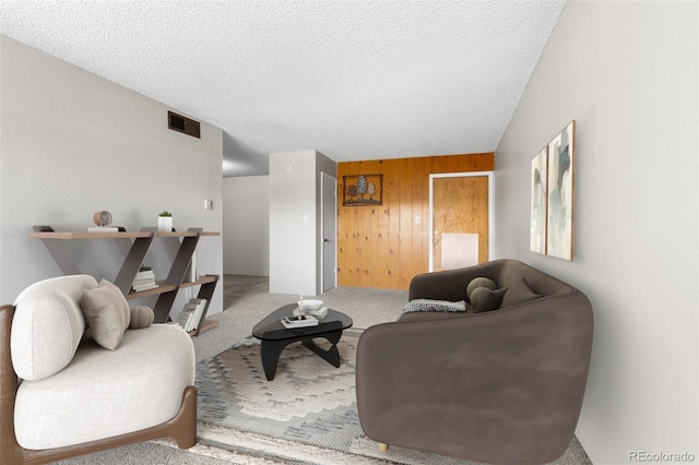 living room featuring carpet, wooden walls, visible vents, and a textured ceiling