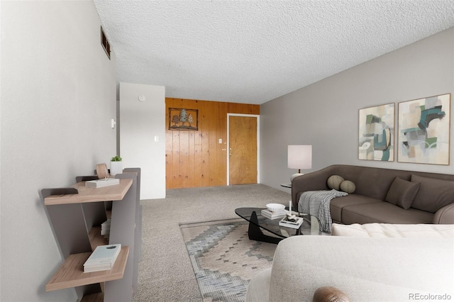 living area with carpet, visible vents, wooden walls, and a textured ceiling