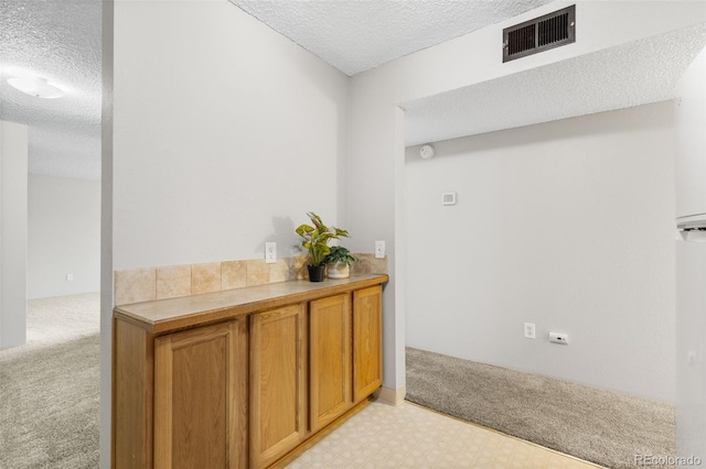 interior space with a textured ceiling, light floors, light carpet, and visible vents