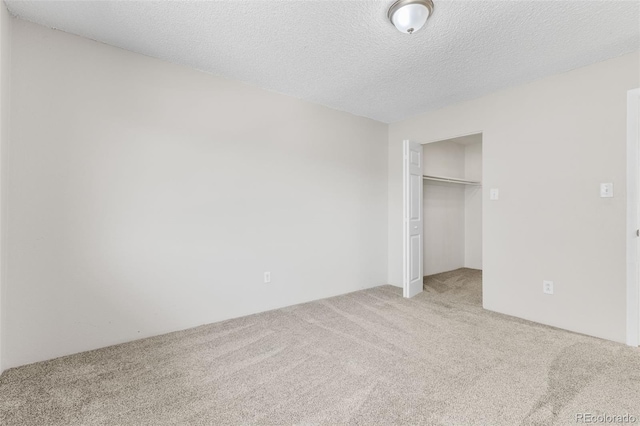 unfurnished bedroom with a closet, a walk in closet, a textured ceiling, and light colored carpet