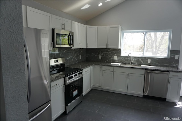 kitchen featuring appliances with stainless steel finishes, a sink, vaulted ceiling, tasteful backsplash, and dark tile patterned flooring