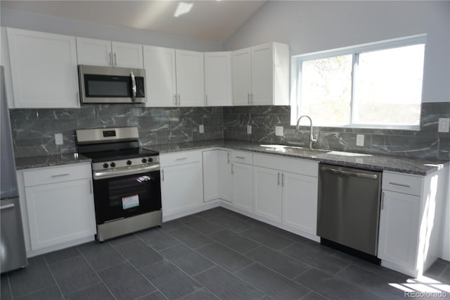 kitchen featuring appliances with stainless steel finishes, a sink, backsplash, vaulted ceiling, and white cabinetry
