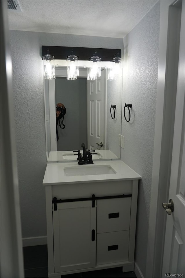 bathroom with vanity, baseboards, a textured wall, and a textured ceiling
