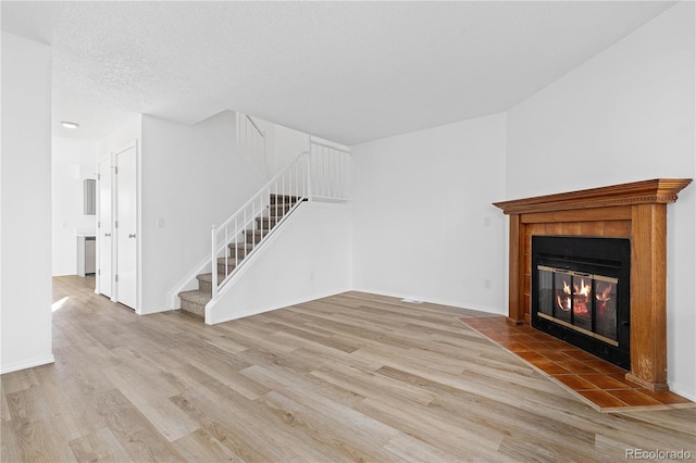 unfurnished living room with stairs, a tile fireplace, a textured ceiling, and wood finished floors