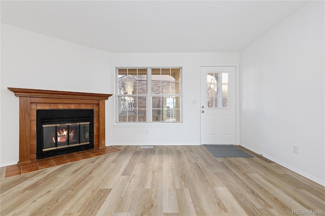 unfurnished living room with visible vents, a fireplace, baseboards, and wood finished floors