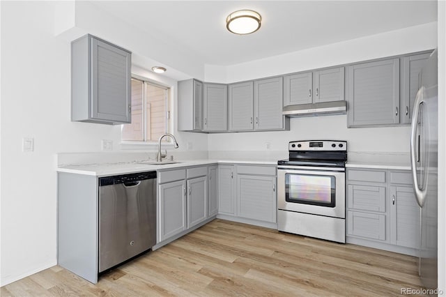 kitchen featuring light wood finished floors, gray cabinets, stainless steel appliances, under cabinet range hood, and a sink