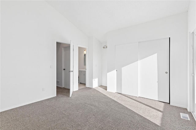 unfurnished bedroom featuring ensuite bathroom, carpet floors, visible vents, vaulted ceiling, and a closet