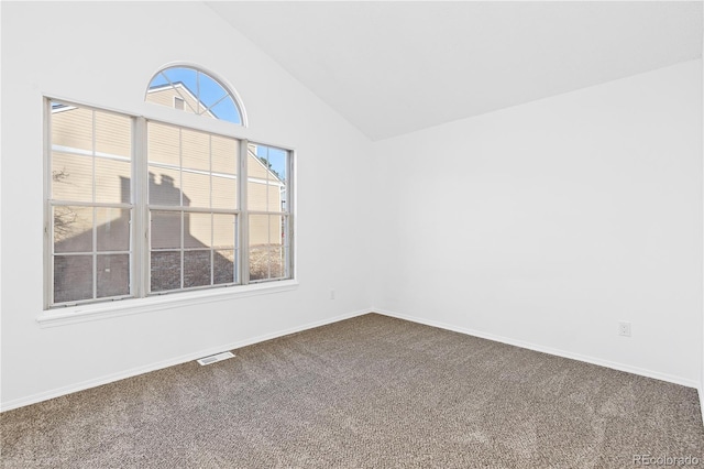 spare room with visible vents, vaulted ceiling, a wealth of natural light, and dark colored carpet