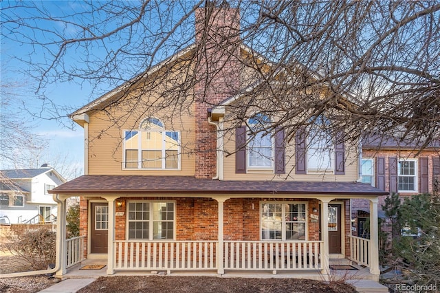 view of front of house featuring a porch, brick siding, a chimney, and roof with shingles