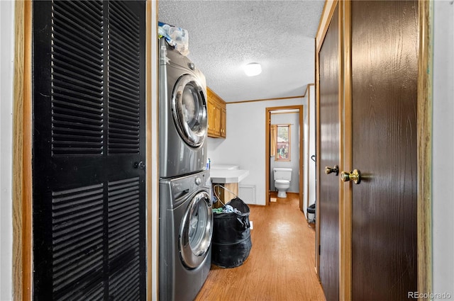 washroom with stacked washing maching and dryer, crown molding, light wood-type flooring, a textured ceiling, and cabinets