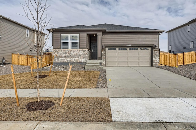 view of front of house featuring an attached garage, fence, stone siding, and driveway