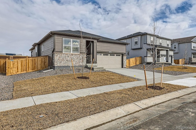 view of front of house featuring a garage, stone siding, driveway, and fence