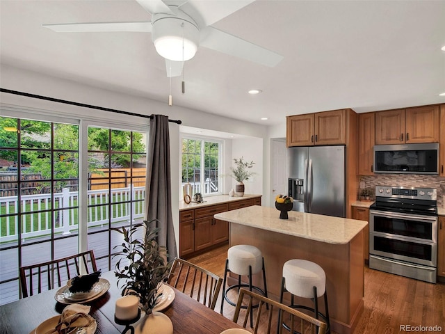 6943 Ingalls St, Arvada, CO 80003 - kitchen featuring appliances with stainless steel finishes, dark wood-style floors, backsplash, brown cabinets, and a kitchen island