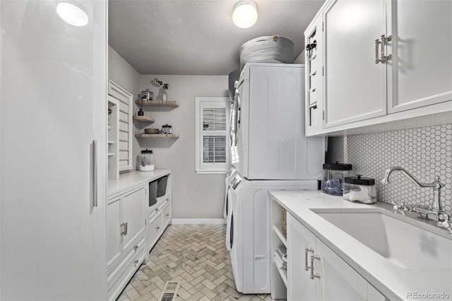 clothes washing area with sink, cabinets, stacked washer / dryer, and a textured ceiling