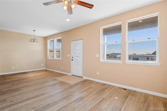 empty room with ceiling fan with notable chandelier, light wood-type flooring, visible vents, and baseboards