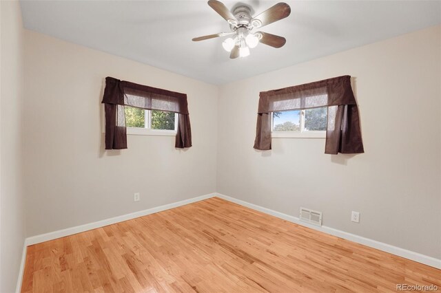 empty room with a wealth of natural light, wood-type flooring, and ceiling fan