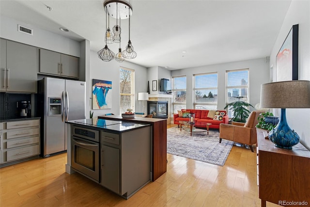 kitchen featuring visible vents, gray cabinetry, stainless steel appliances, dark countertops, and light wood-type flooring