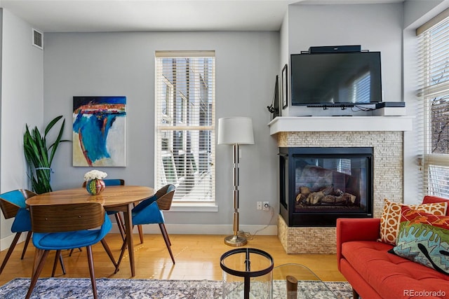 living room featuring visible vents, wood finished floors, a healthy amount of sunlight, and a glass covered fireplace