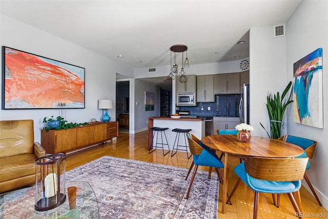 dining room with light wood-type flooring, visible vents, and baseboards