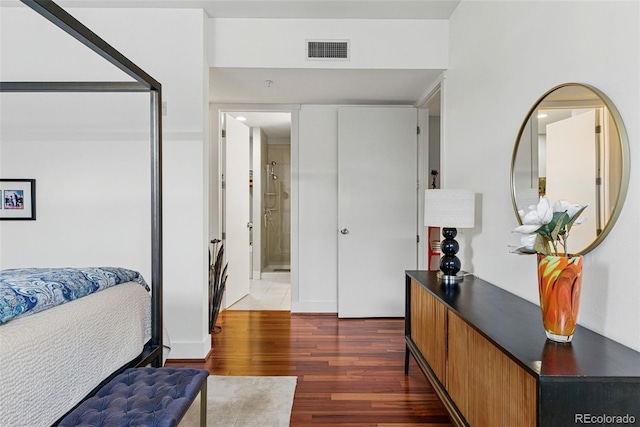 bedroom with connected bathroom, visible vents, and wood finished floors