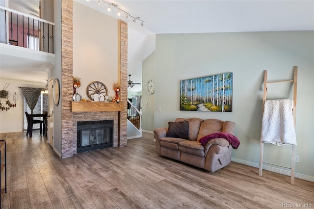 living room with rail lighting, ceiling fan, high vaulted ceiling, hardwood / wood-style floors, and a stone fireplace