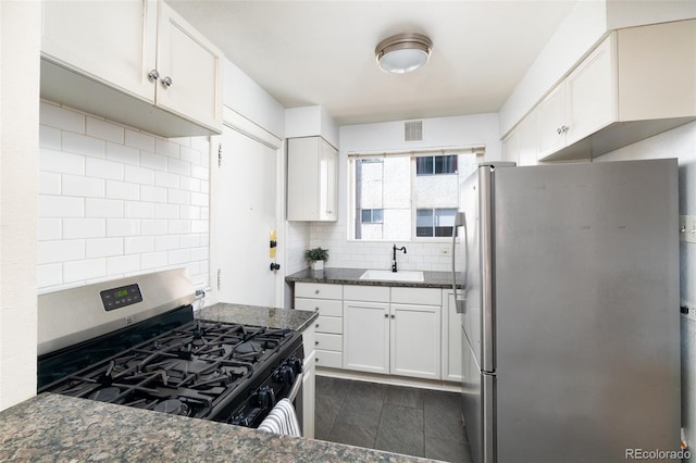 kitchen with tasteful backsplash, sink, dark stone counters, white cabinetry, and appliances with stainless steel finishes