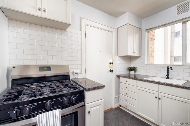 kitchen with sink, white cabinetry, stainless steel gas range oven, dark stone counters, and decorative backsplash