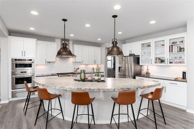 kitchen featuring tasteful backsplash, white cabinets, a warming drawer, a kitchen island with sink, and stainless steel appliances