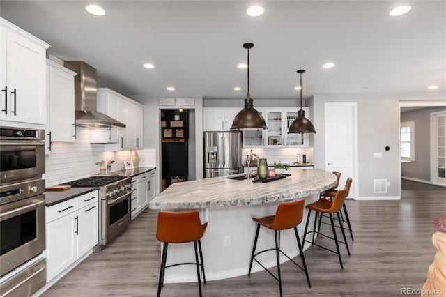 kitchen with visible vents, wall chimney exhaust hood, a warming drawer, stainless steel appliances, and decorative backsplash