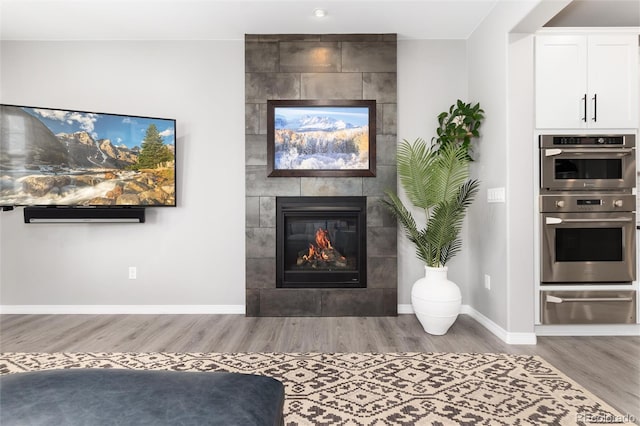 living room featuring baseboards, a tile fireplace, and wood finished floors