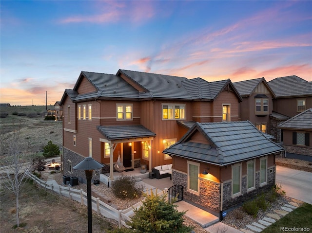 rear view of house with a tile roof, stone siding, a patio area, and fence private yard