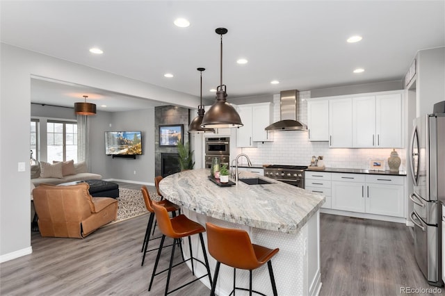 kitchen with baseboards, wall chimney range hood, appliances with stainless steel finishes, a sink, and wood finished floors