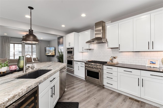 kitchen with a sink, decorative backsplash, white cabinetry, wall chimney exhaust hood, and appliances with stainless steel finishes