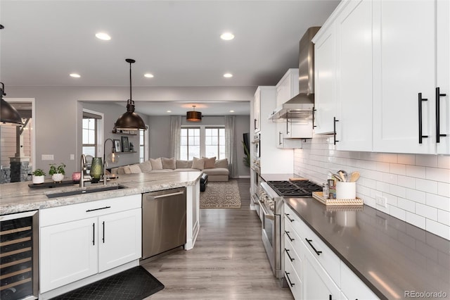 kitchen with wall chimney exhaust hood, open floor plan, recessed lighting, stainless steel appliances, and beverage cooler