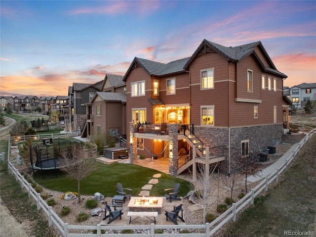rear view of house featuring a fenced backyard, stone siding, a trampoline, stairway, and an outdoor fire pit