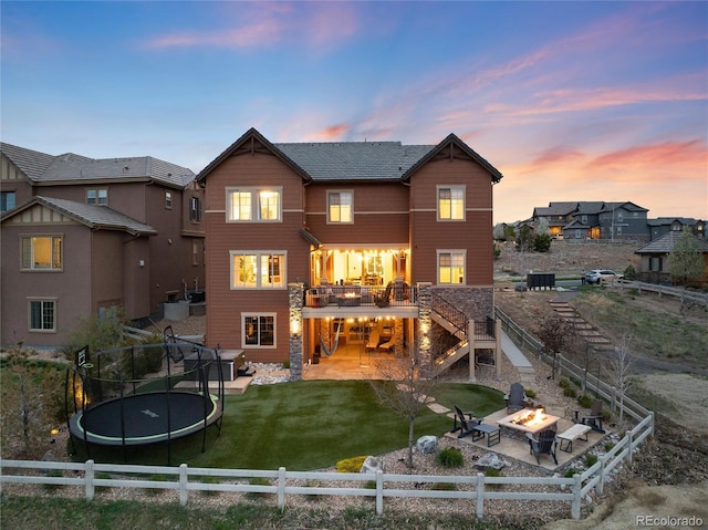 back of property at dusk featuring a patio, a fenced backyard, a fire pit, and a trampoline
