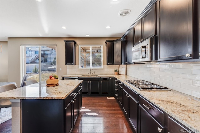 kitchen featuring visible vents, dark wood-type flooring, light stone countertops, appliances with stainless steel finishes, and a sink