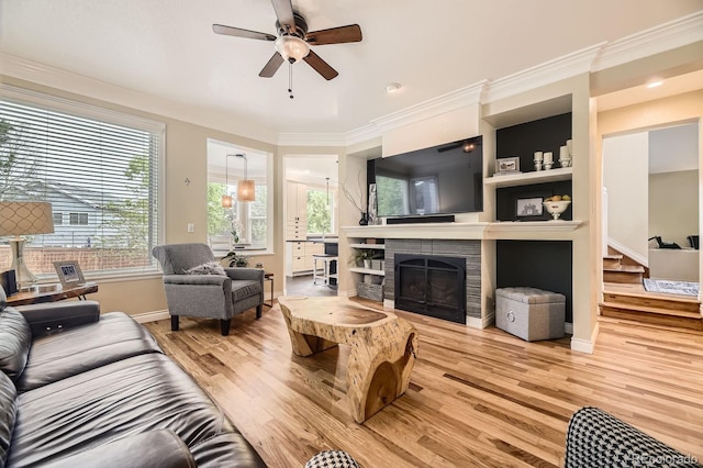 8657 Aberdeen Cir, Highlands Ranch, CO 80130 - living area featuring light wood finished floors, a ceiling fan, a tiled fireplace, crown molding, and baseboards