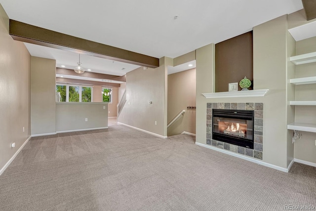 2943 W Riverwalk Cir Unit I, Littleton, CO 80123 - unfurnished living room featuring carpet flooring, a tiled fireplace, beam ceiling, stairs, and built in shelves