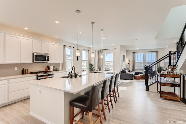 kitchen featuring a sink, stainless steel appliances, a center island with sink, light wood finished floors, and light countertops