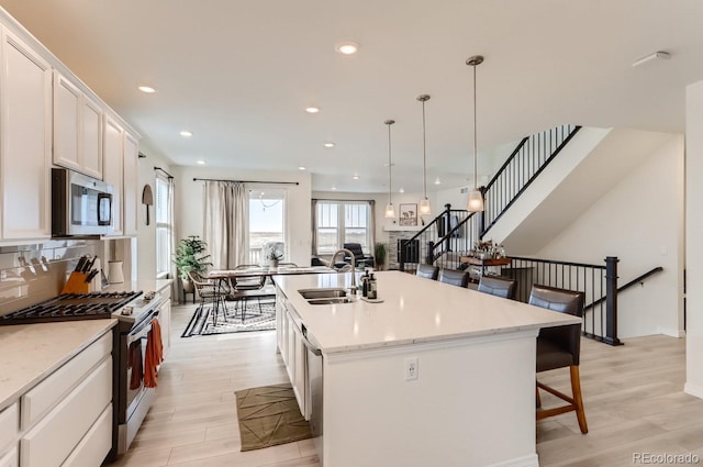 kitchen with a breakfast bar area, a sink, stainless steel appliances, white cabinets, and a center island with sink